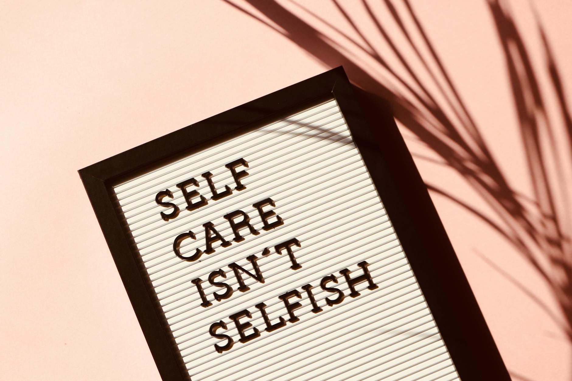 pexels-photo-2821823-2821823 Letter board displaying 'Self Care Isn't Selfish' with artistic shadow on pink background.